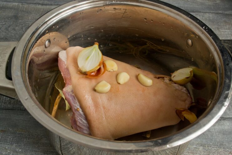 Step 3: Adding Onion and Garlic for a Flavorful Broth Chopped onion and garlic cloves being added to the pot with the pork knuckle.