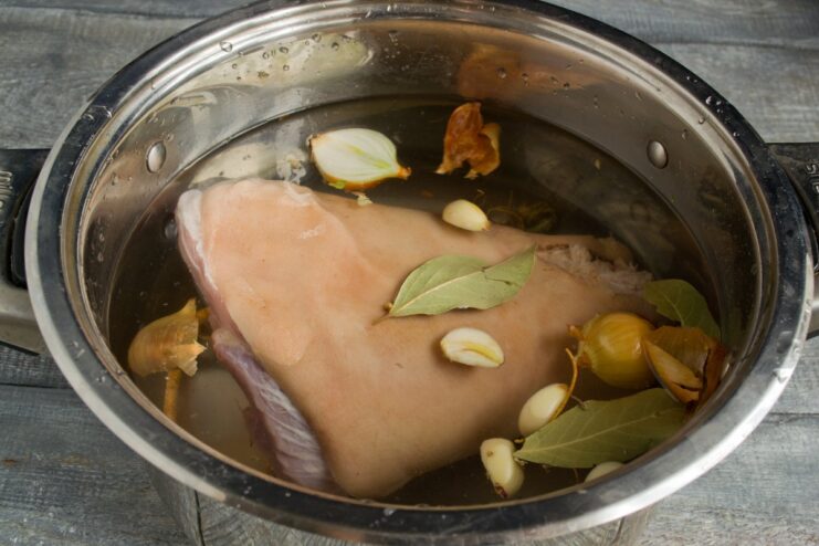 Step 4: Covering the Pork Knuckle with Water for Simmering A pot with a pork knuckle and vegetables being filled with cold water.