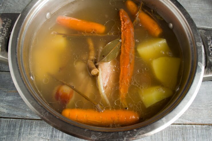 Step 6: Adding Potatoes and Carrots to the Pot Peeled potatoes and carrots being added to the pot with the simmering pork knuckle.