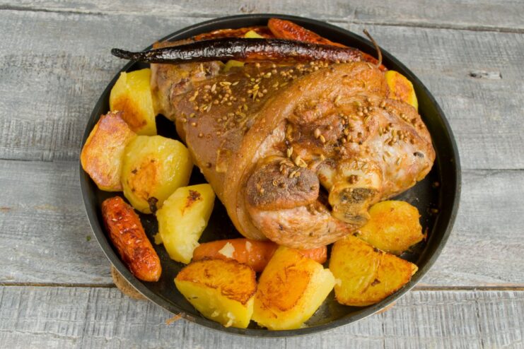 The Final Step: Roasting to Perfection for a Crispy Skin A baking dish in the oven with a pork knuckle and potatoes roasting to a golden-brown color.