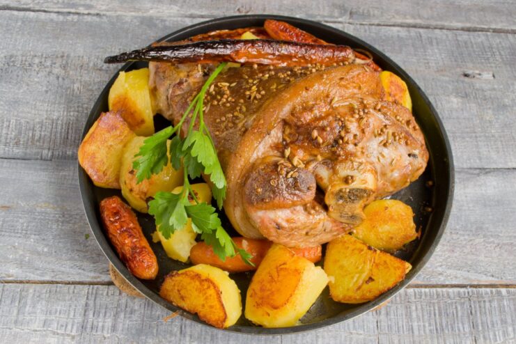 The Finished Dish: A Stunning Centerpiece for Your Celebration A beautifully roasted pork knuckle with potatoes and herbs served on a platter.