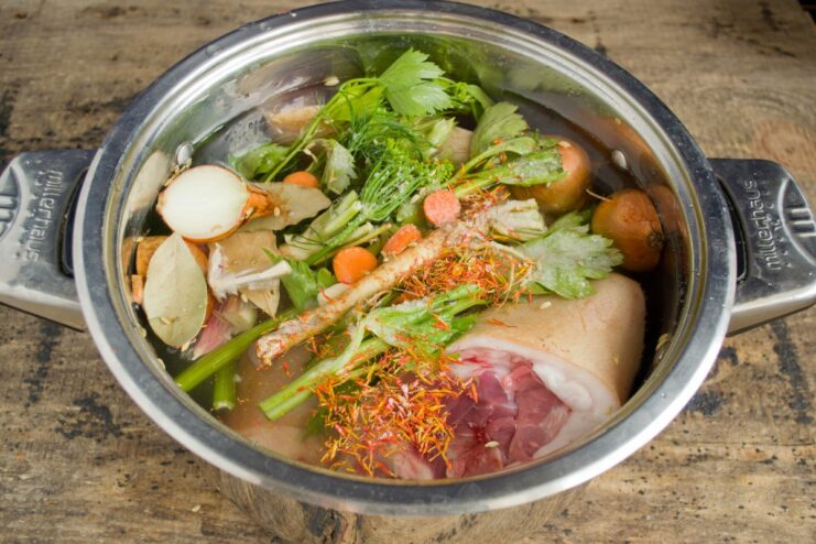 The Secret to Tenderness: Pouring in Beer and Water Pouring light beer from a bottle into the pot with pork knuckles and vegetables.