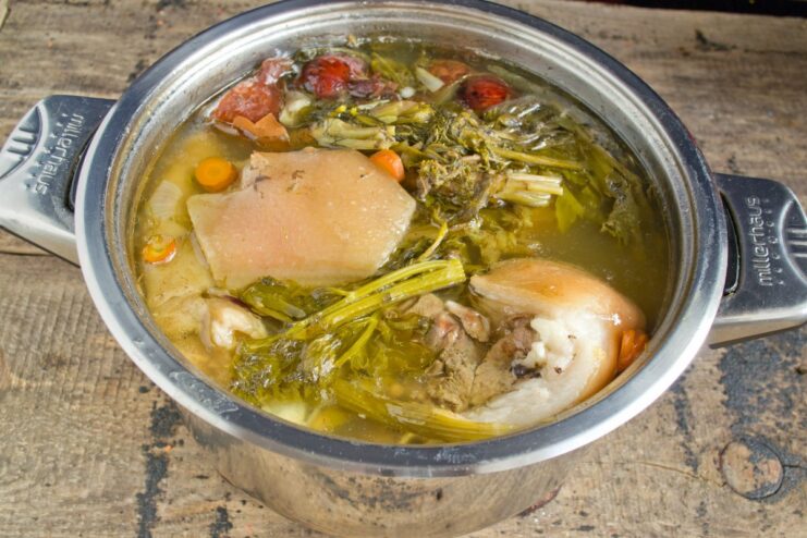 Slow Simmering the Pork Knuckle for Maximum Tenderness A large pot on the stove with pork knuckle simmering in a dark broth.