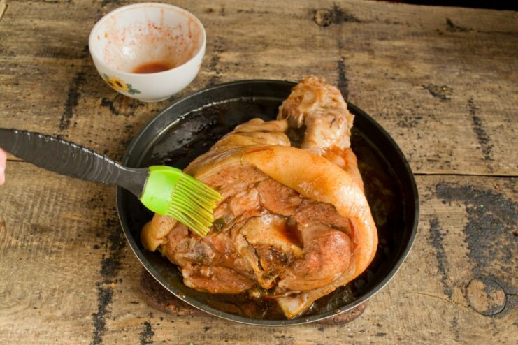 Creating a Crispy Skin: Brushing with a Flavorful Glaze A hand using a pastry brush to apply a red glaze to a boiled pork knuckle.