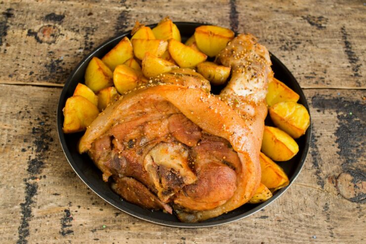 The Perfect Pairing: Serving Pork Knuckle with Potatoes and Beer A perfectly cooked pork knuckle served on a plate with a side of fried potatoes and a glass of beer.