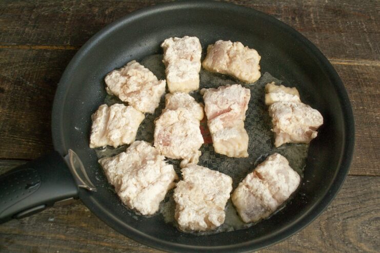 Frying the breaded fish fillets until they are golden and crispy Flour-coated hake fillets frying to a golden-brown color in a hot skillet.