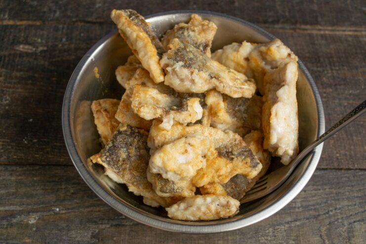 Placing fried fish on a paper towel to remove excess oil Golden-fried pieces of hake resting on a paper towel to drain excess oil.