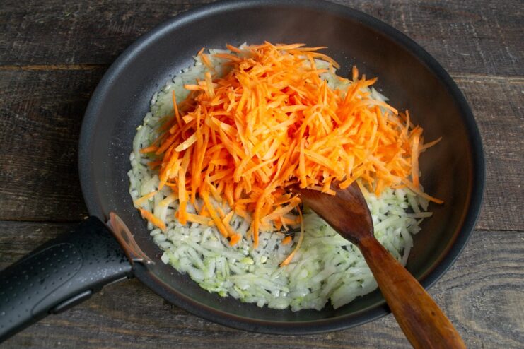 Sautéing onions and carrots to create the base for the vegetable marinade Sautéing chopped onions and grated carrots in a skillet for the marinade.