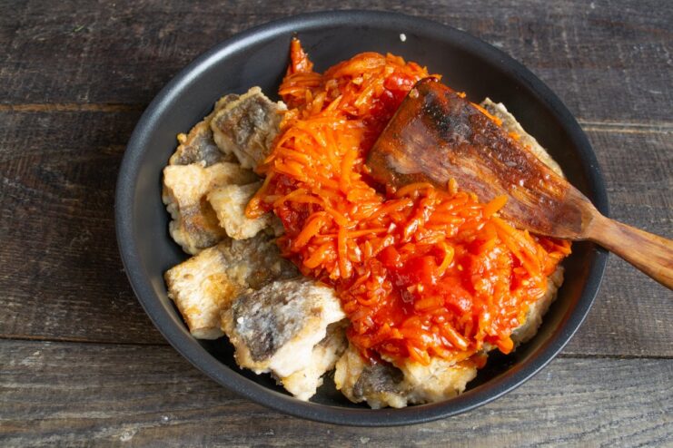 Combining the fried fish with the vegetable marinade in a skillet Fried fish fillets being covered with the carrot and onion marinade in a skillet.