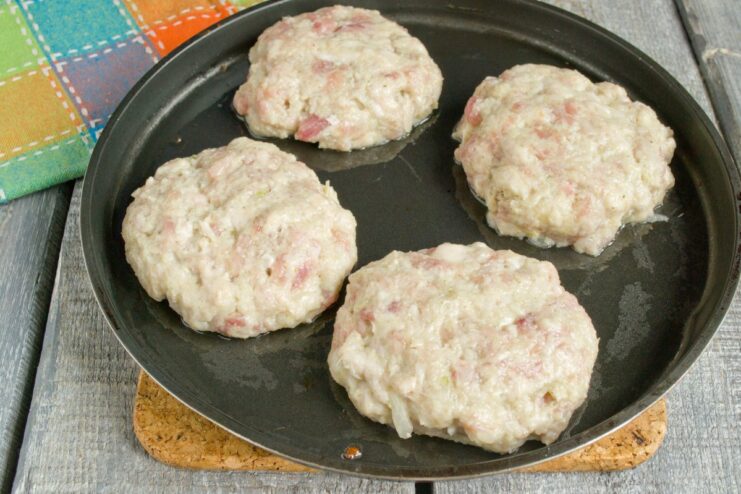 Frying the Pork Patties to Perfection Hand-formed raw pork patties being placed into a hot skillet with oil.