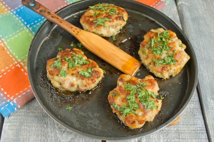 Golden-Brown Pork Patties Simmering in a Pan Pork patties being fried to a golden-brown crust on both sides in a skillet.
