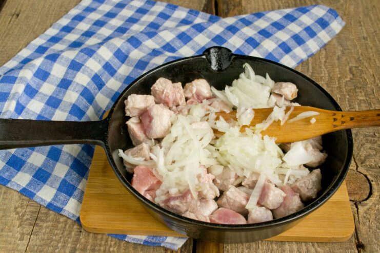 Frying meat with chopped onions and garlic Diced meat, onions, and garlic being sautéed together in a pan.