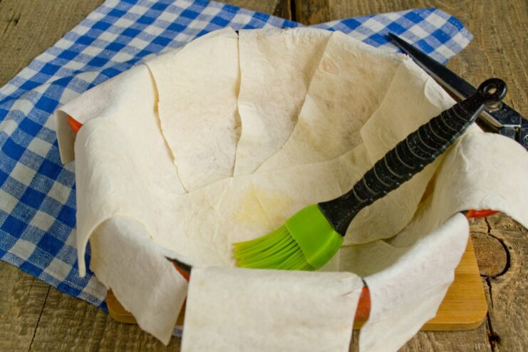 Lining a cast-iron pot with buttered lavash strips A cast-iron pot being lined with overlapping strips of lavash.