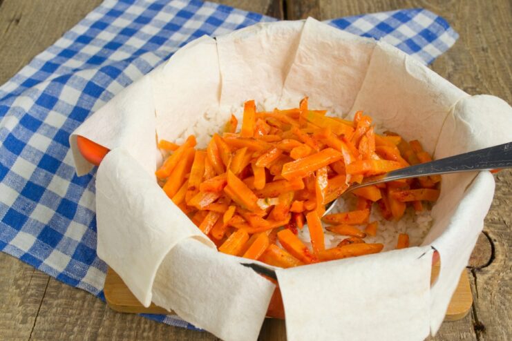 Layering sautéed carrots over the rice A layer of cooked carrots being spread over the rice in the pot.