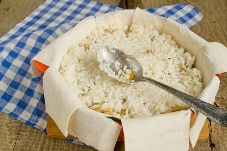 Adding the final layer of rice and drizzling with butter The final layer of rice being added, with melted butter poured on top.