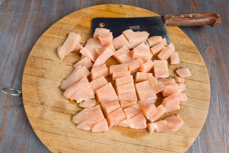Chopping Chicken Fillet by Hand for the Perfect Schnitzel Texture Close-up of finely chopped chicken fillet on a wooden cutting board with a large knife.