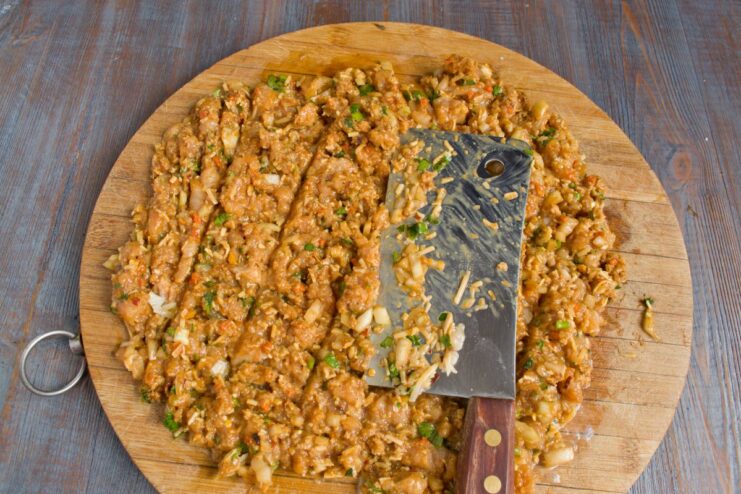 Using a Cleaver to Combine and Mince All Ingredients Together A cleaver chopping the chicken mixture on a cutting board to combine all ingredients.