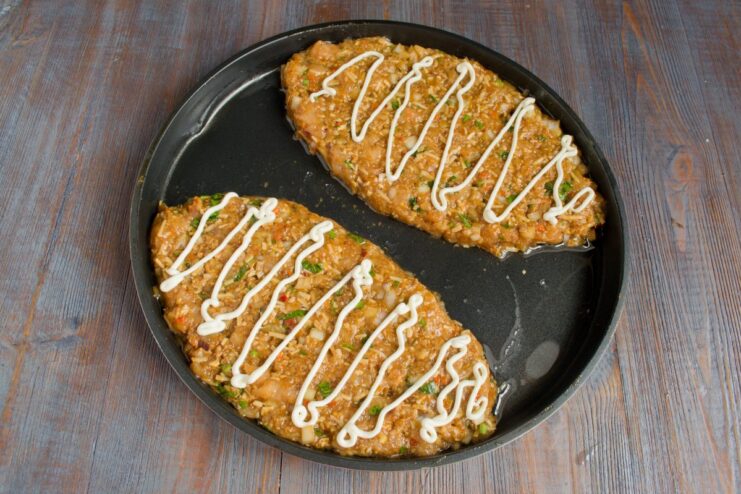 Shaping the Chopped Chicken Schnitzels Directly in the Baking Pan Two large, flat chicken patties being formed in a non-stick pan, ready for baking.