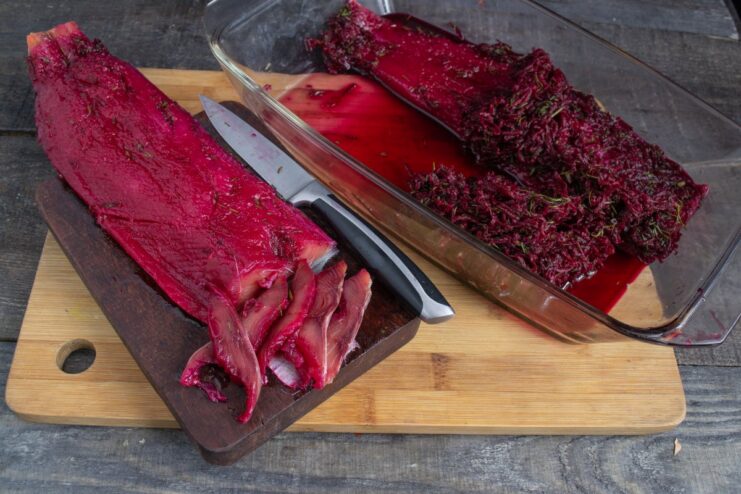 How to Slice Beetroot Gravlax Perfectly A cured beetroot gravlax fillet being thinly sliced with a sharp knife on a cutting board.