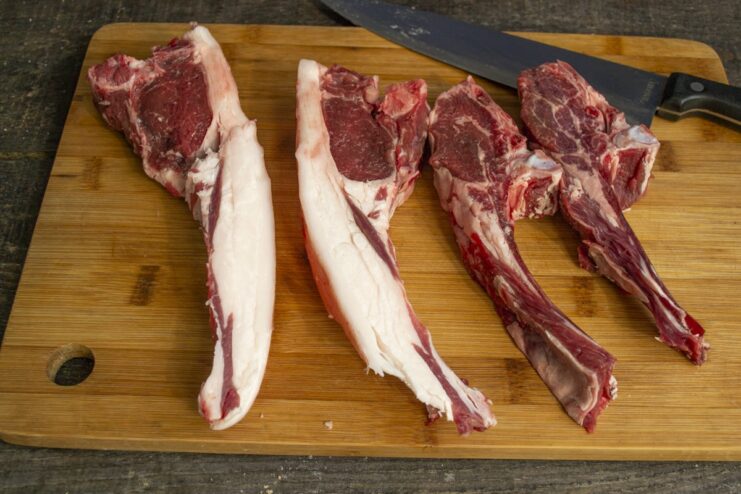 Step 1: Always pat lamb chops dry for a perfect sear Raw lamb chops being patted dry with a paper towel on a wooden board.