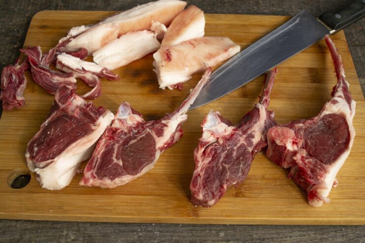Trimming the lamb chops before cooking A hand with a knife trimming excess fat from raw lamb chops.