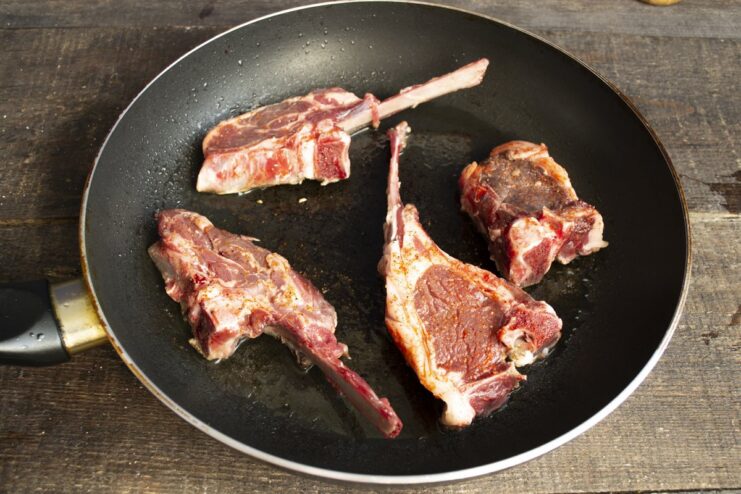 Searing the lamb chops for a beautiful golden-brown crust Two lamb chops searing in a hot skillet to create a golden crust.