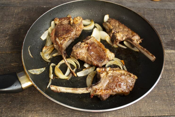 Finishing the lamb chops in the oven for a juicy result Skillet with lamb chops and onions inside an oven.