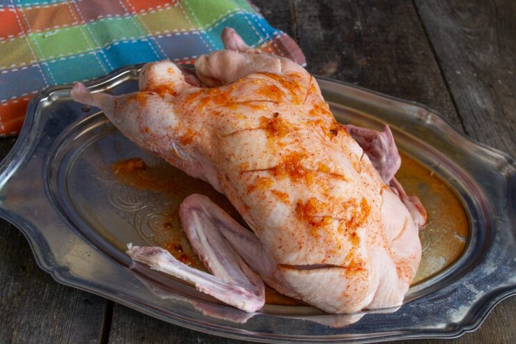 Marinating the Duck with Citrus and Spices A hand rubbing a golden-colored marinade over a raw duck.