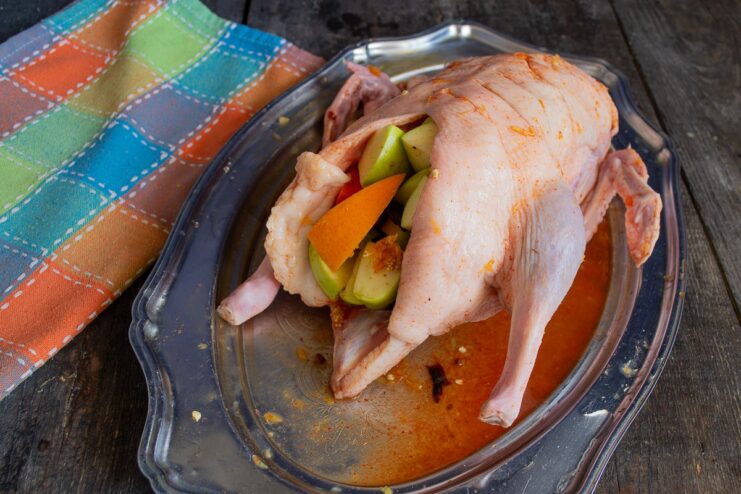 Stuffing the Duck with the Fruit and Vegetable Mixture A raw duck being filled with a colorful stuffing of oranges, apples, and carrots.