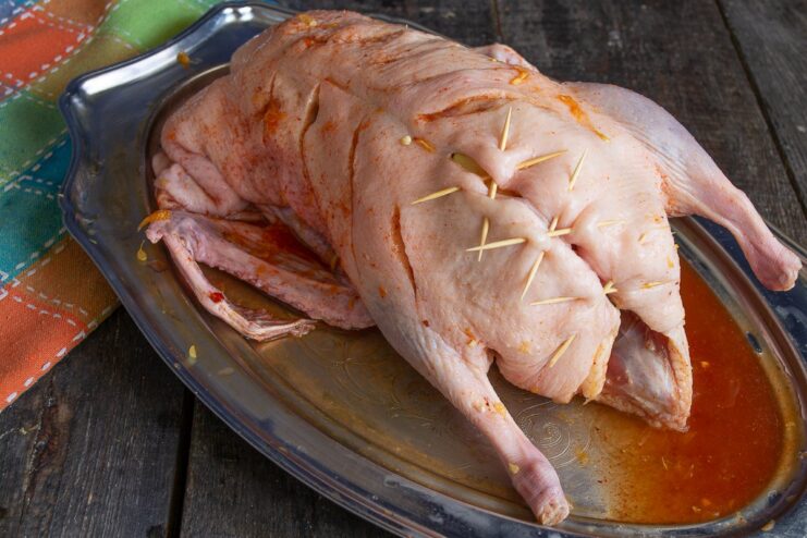 Securing the Duck Cavity with Skewers Closing the duck's cavity with wooden skewers to hold the stuffing inside.