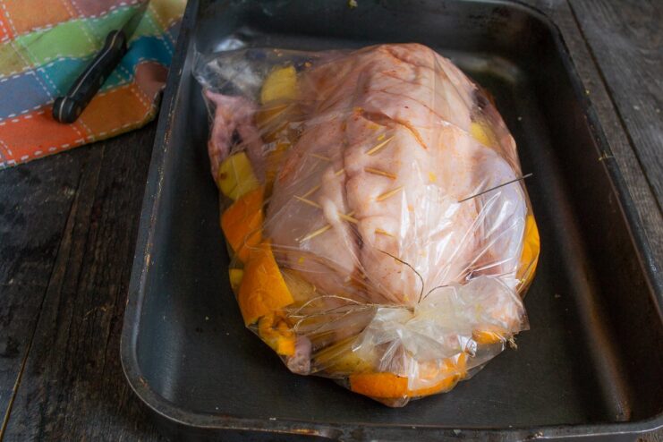 Placing the Stuffed Duck in a Roasting Bag A stuffed duck being placed into a clear roasting bag with orange slices.