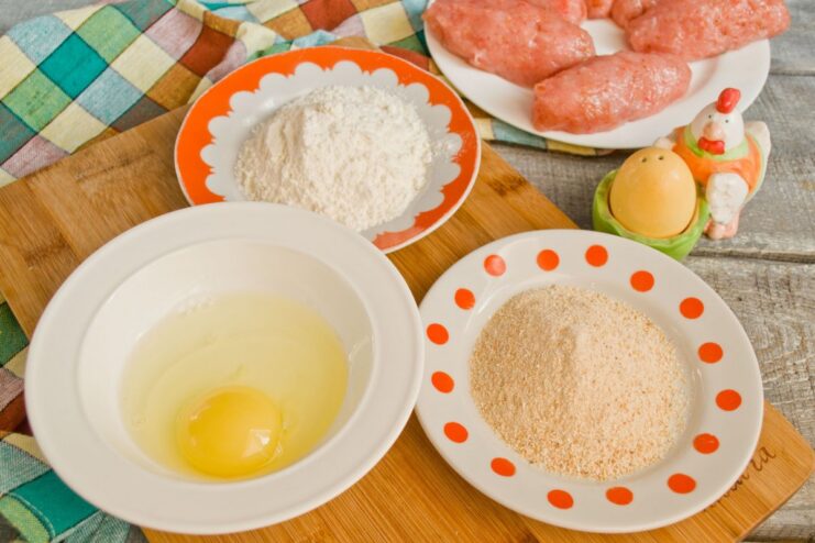 The three-step breading station: flour, egg, and breadcrumbs Three plates set up for breading: one with flour, one with a beaten egg, and one with breadcrumbs.
