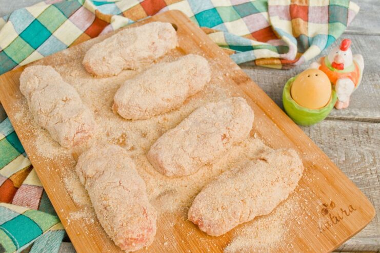 Chilling the breaded cutlets helps the coating adhere better during frying Breaded, uncooked chicken cutlets arranged on a board, ready for chilling.