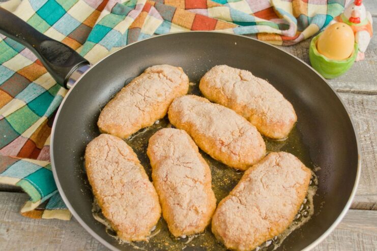 Frying chicken cutlets in ghee until golden brown and crispy Chicken cutlets sizzling in a pan with melted ghee, turning golden brown.