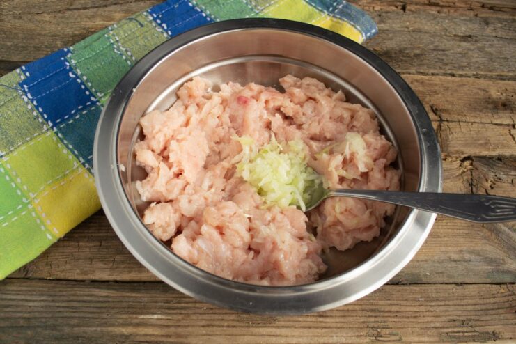 Adding Grated Onion for Extra Juiciness in Chicken Cutlets A bowl of minced chicken with freshly grated onion being added to the mixture.