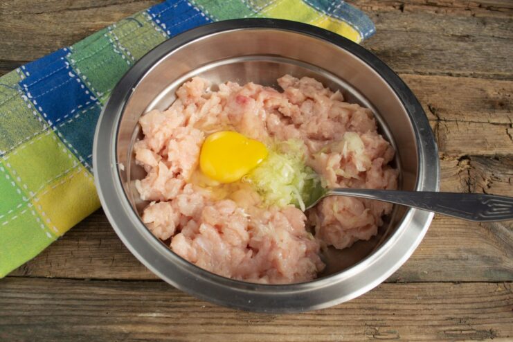 The Key Ingredients for Binding and Moisture: Egg, Salt, and Water A raw egg, salt, and ice-cold water being added to the minced chicken mixture in a bowl.