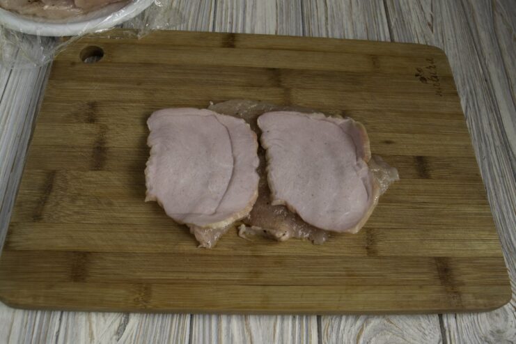 A thin slice of ham being placed on top of a pounded chicken fillet.