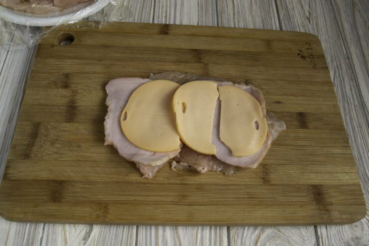 Thin slices of cheese being layered over the ham on a chicken fillet.