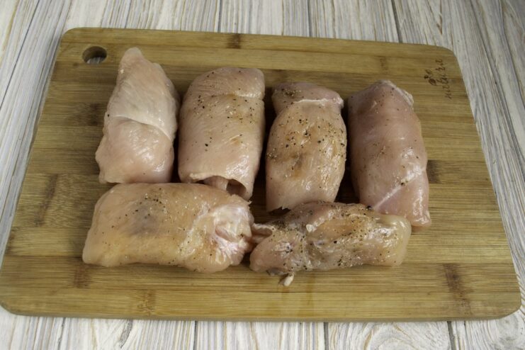 A chicken fillet with ham and cheese being tightly rolled up to form a Cordon Bleu roll.
