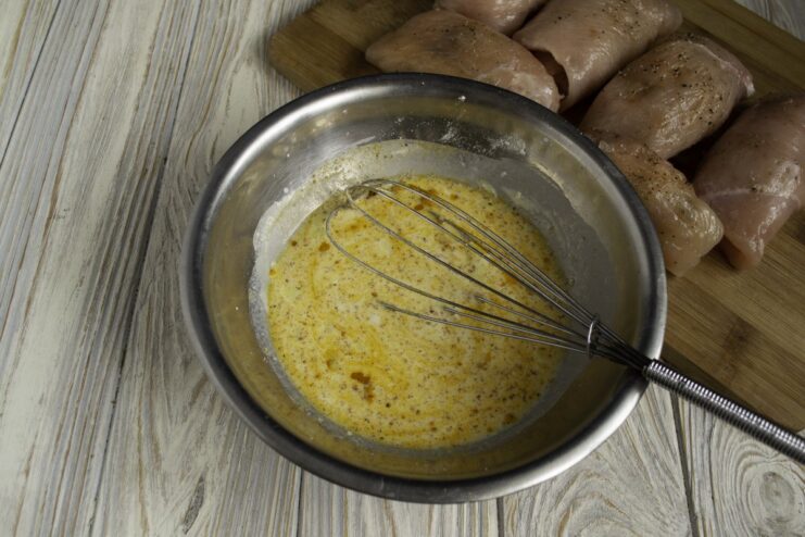 A bowl with flour, cream, broth, and spices being whisked to create the béchamel sauce.