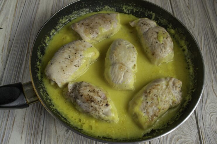 Chicken Cordon Bleu rolls simmering in a creamy béchamel sauce in a skillet.