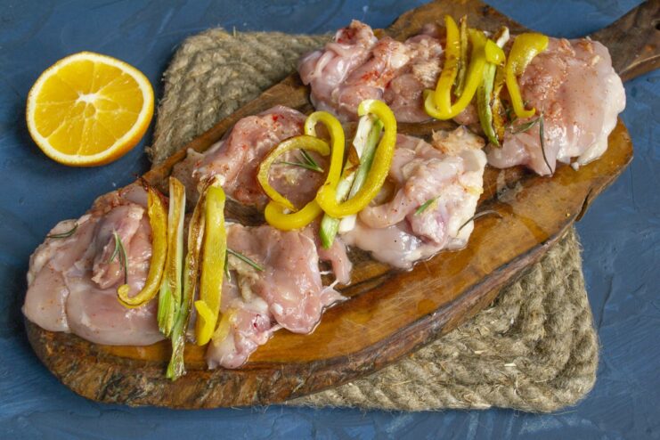 Adding the sautéed vegetable filling to the marinated chicken. A flattened chicken thigh topped with sautéed bell peppers and scallions.
