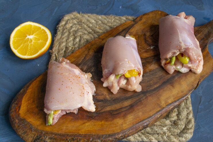 Rolling the chicken thigh tightly around the vegetable filling. A hand rolling a chicken thigh with vegetable filling into a neat roll.