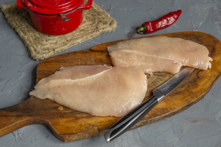 Preparing the chicken: pounding and seasoning the fillets before breading. Two raw chicken fillets on a cutting board being seasoned with salt.