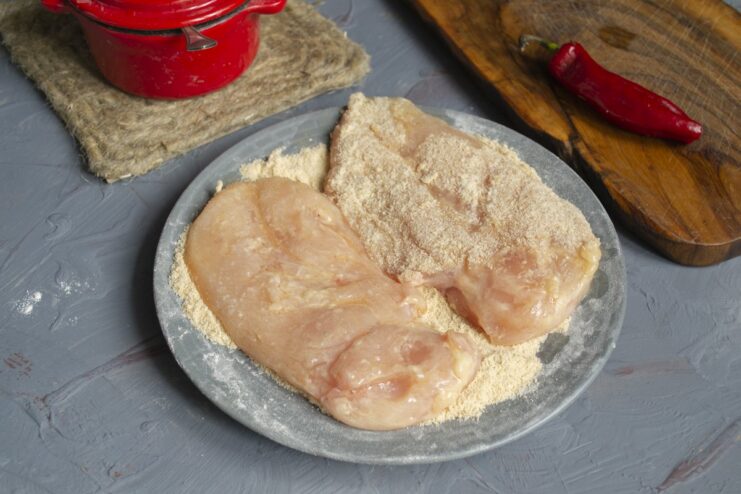 The final breading step: coating the egg-washed chicken in breadcrumbs for a crispy finish. A chicken fillet being coated in breadcrumbs after being dipped in egg.