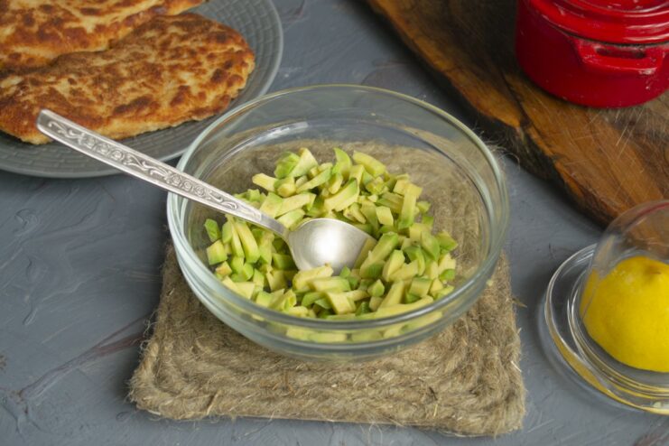 Preparing the avocado salsa: dicing the avocado and adding lemon juice to prevent browning. A bowl of diced avocado with lemon juice being squeezed over it.