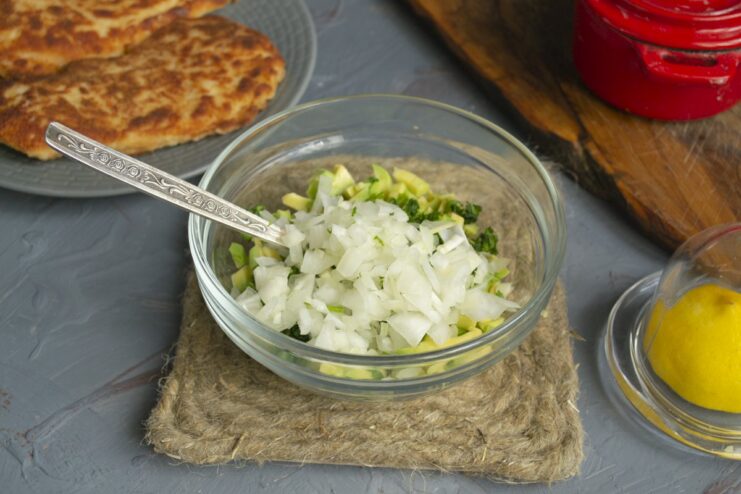 Adding finely diced onion to the avocado salsa mix. Finely diced onion being added to the bowl with avocado and cilantro.