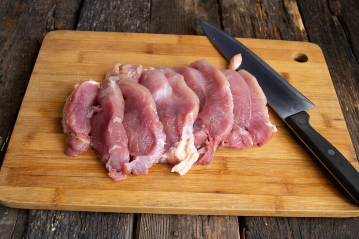 Preparing the Pork Tenderloin for Schnitzel Slices of raw pork tenderloin on a cutting board, being patted dry with a paper towel.
