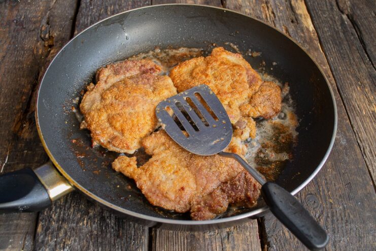 Finishing the Schnitzel - Crispy and Golden on Both Sides A perfectly golden-brown pork schnitzel being flipped in a pan to cook the other side.