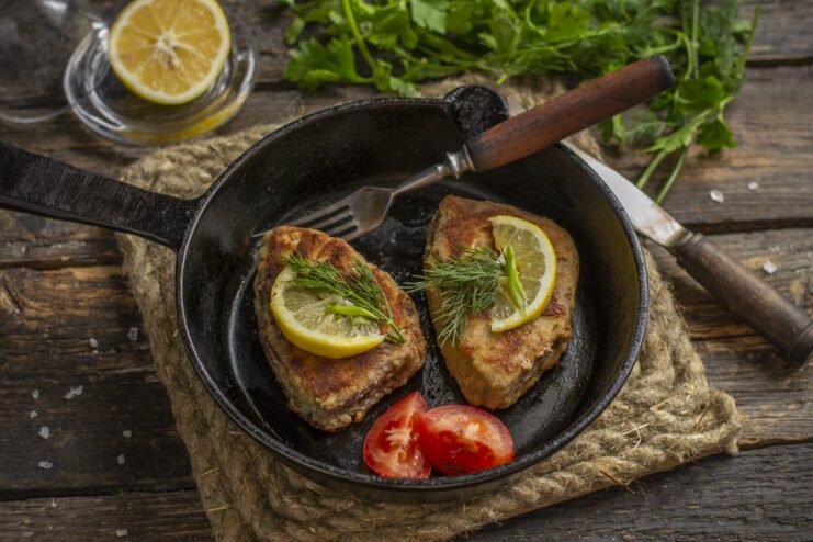 A plate with a ready-to-eat juicy pan-fried breaded tuna steak, garnished with a lemon slice.